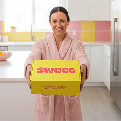 THE SWEETUAL™ — woman in a pink robe holding the yellow shipping box in her kitchen