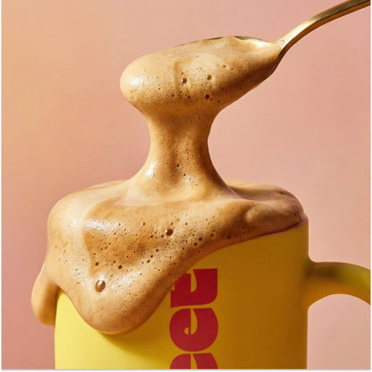 THE SWEETUAL™ — coffee foam overflowing a mug as a spoon lifts a peak of foam against a pink background
