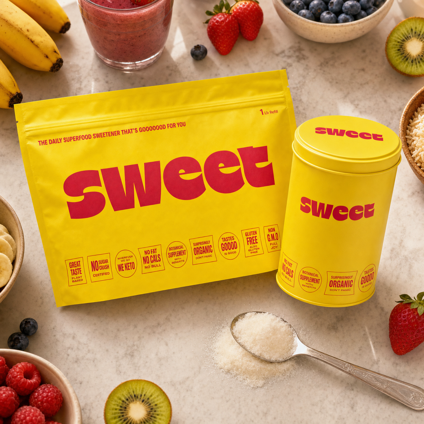Overhead view of a SWEET refill pouch and tin on a counter with bananas, berries, kiwi and a smoothie