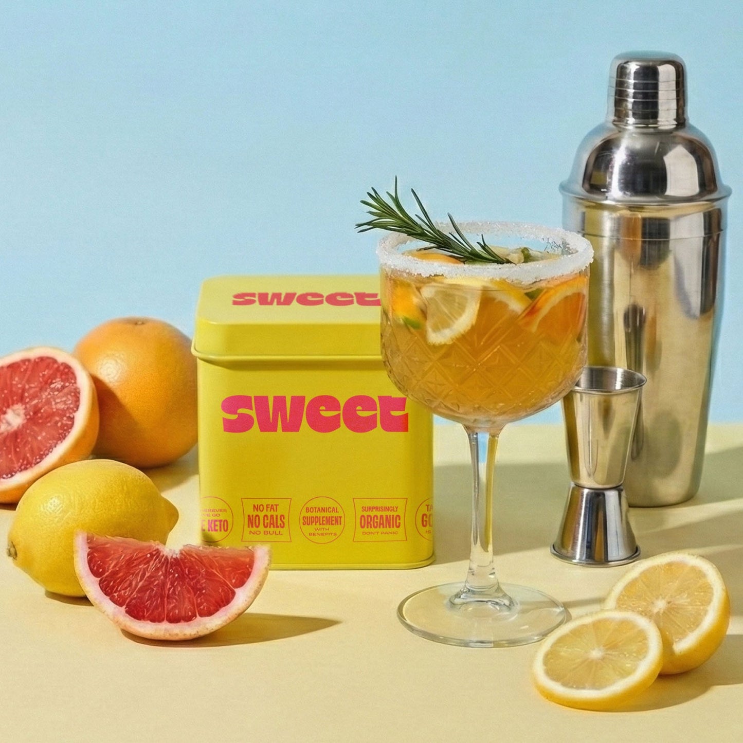 SWEET square tin beside a citrus cocktail with rosemary garnish, shaker, and fresh grapefruit