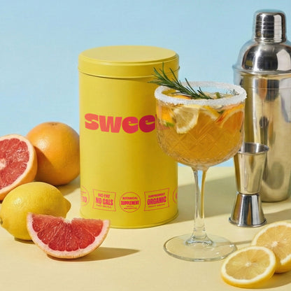 SWEET tin beside a citrus cocktail with rosemary garnish, shaker, and fresh grapefruit